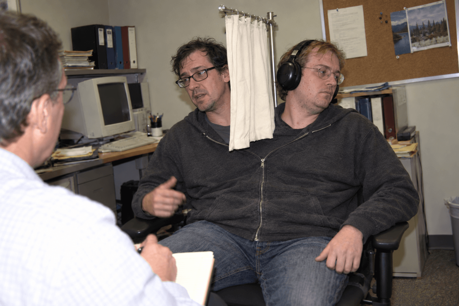 A FullStack Genetics specialist in a one-on-one with their manager. A privacy curtain and over-ear headphones separate them from their conjoined colleague.